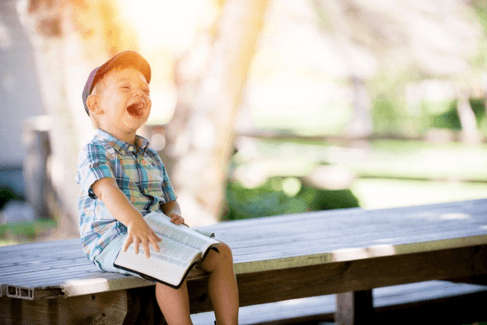 photo of a young boy with a book laughing