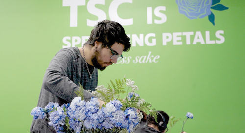 A student in front of TSC Is Spreading Petals logo working on an arrangement